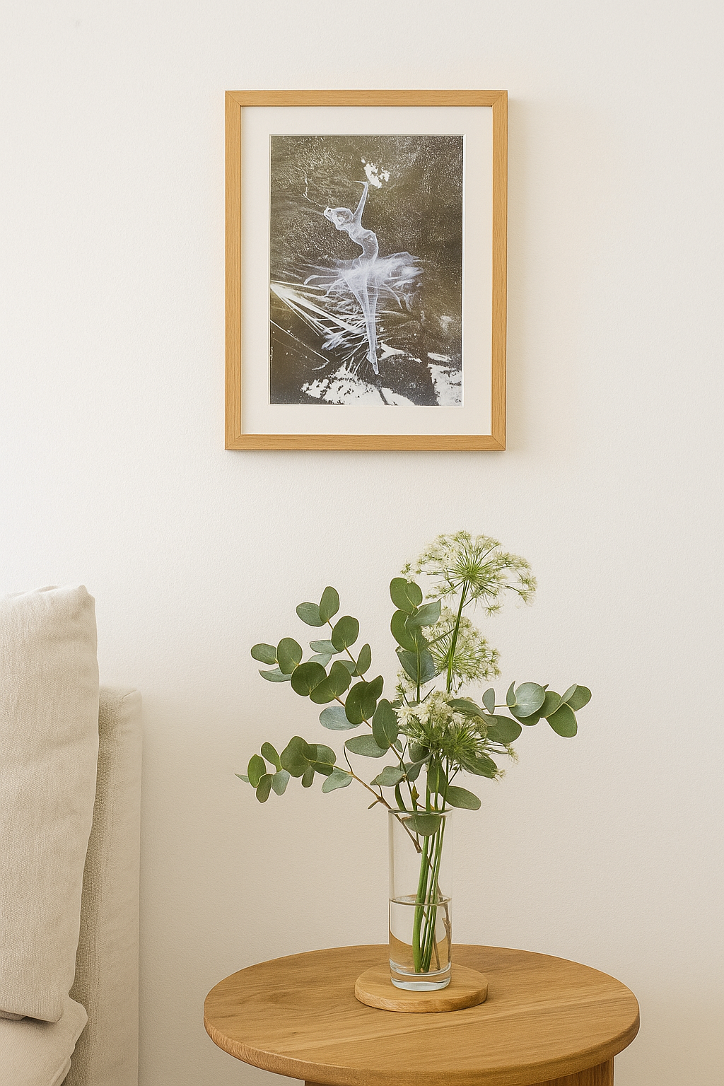 Framed artwork above a vase with greenery on a wooden table against a white wall. Artwork by Guido Salimbeni